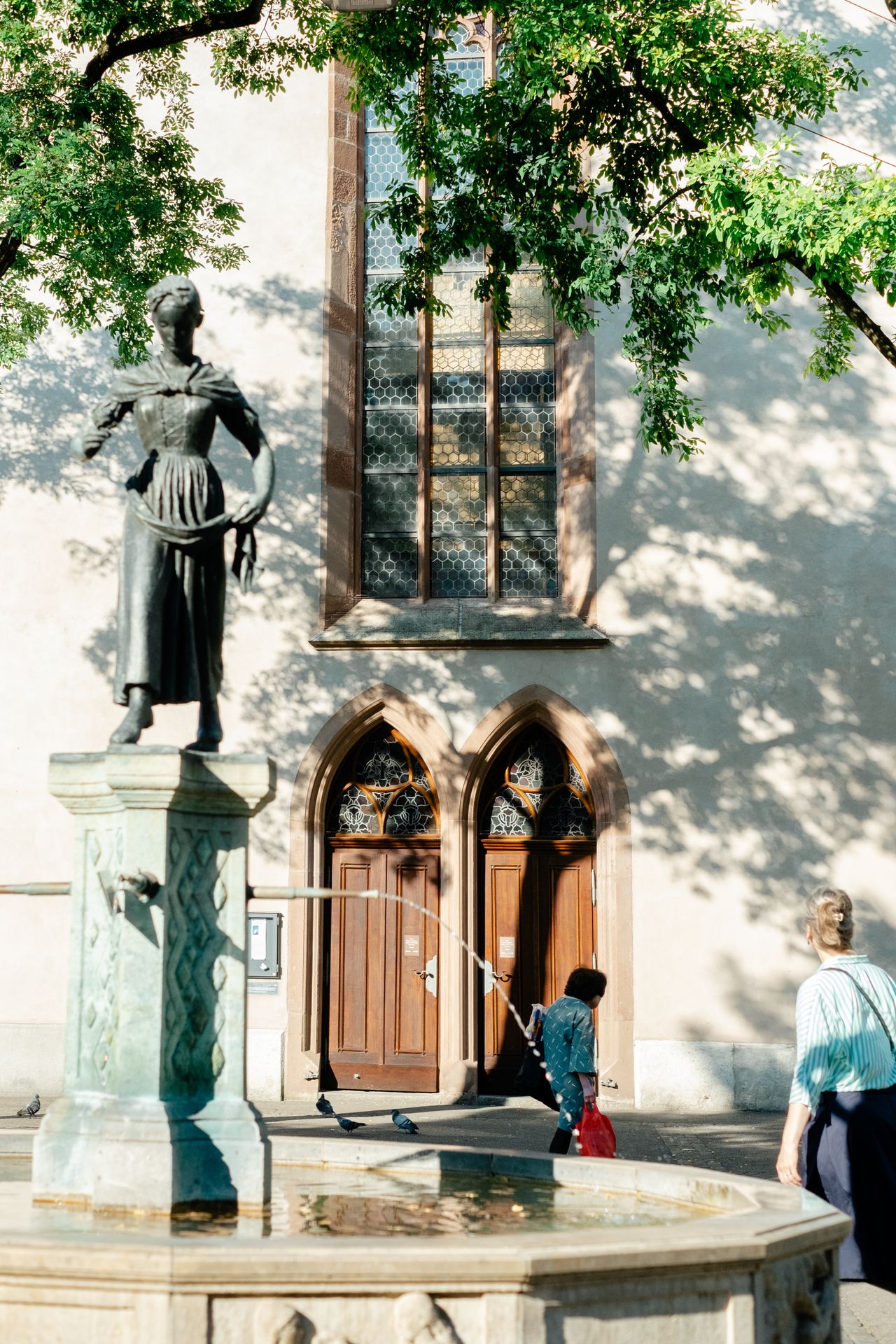 People are photographed out in the sunshine in a Swiss town characterized by beautiful architecture, lush greenery, and art installations.