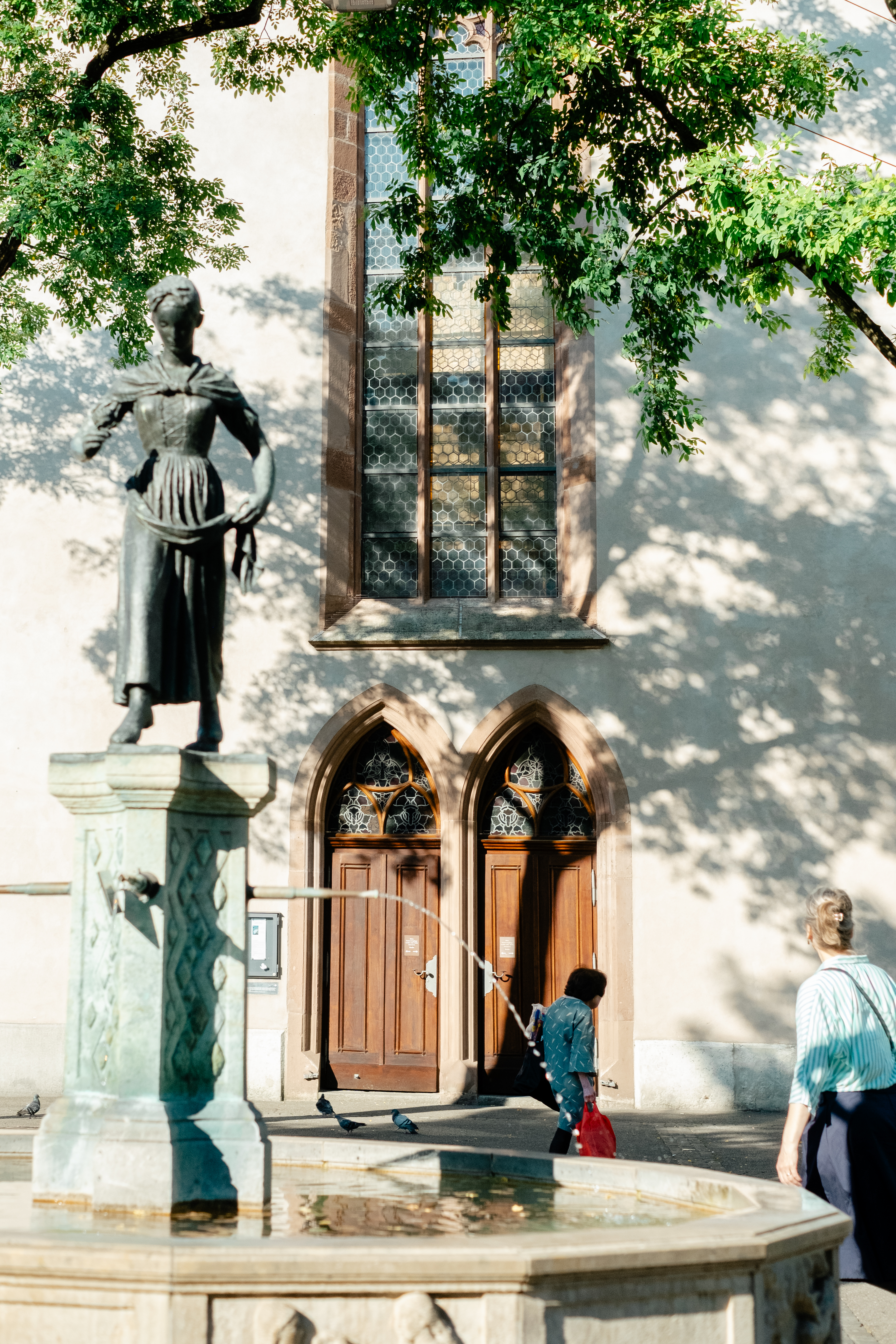 People are photographed out in the sunshine in a Swiss town characterized by beautiful architecture, lush greenery, and art installations.