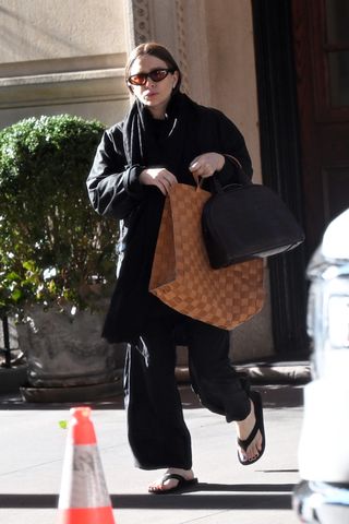 A photo of Ashley Olsen styling two bags from The Row with the brand's black leather flip flops.