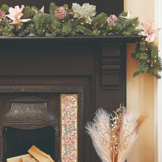 A black fireplace decorated for Christmas with a light-up garland with pink flowers