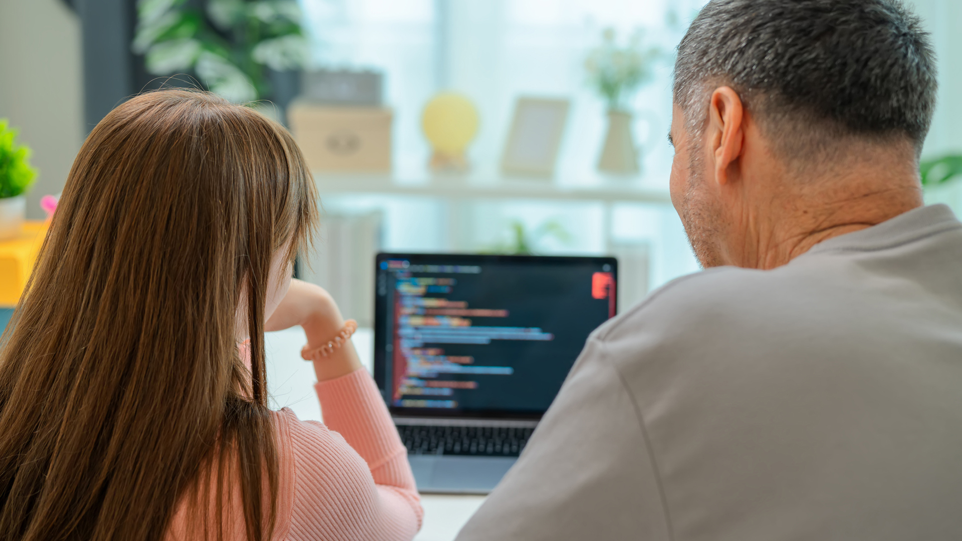 A grandfather and his grandaughter both look at the same laptop screen