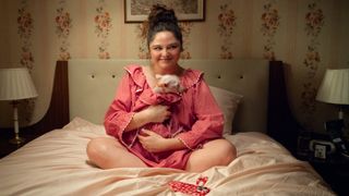 Jess and Astrid in matching pink outfits sitting on a bed in Too Much