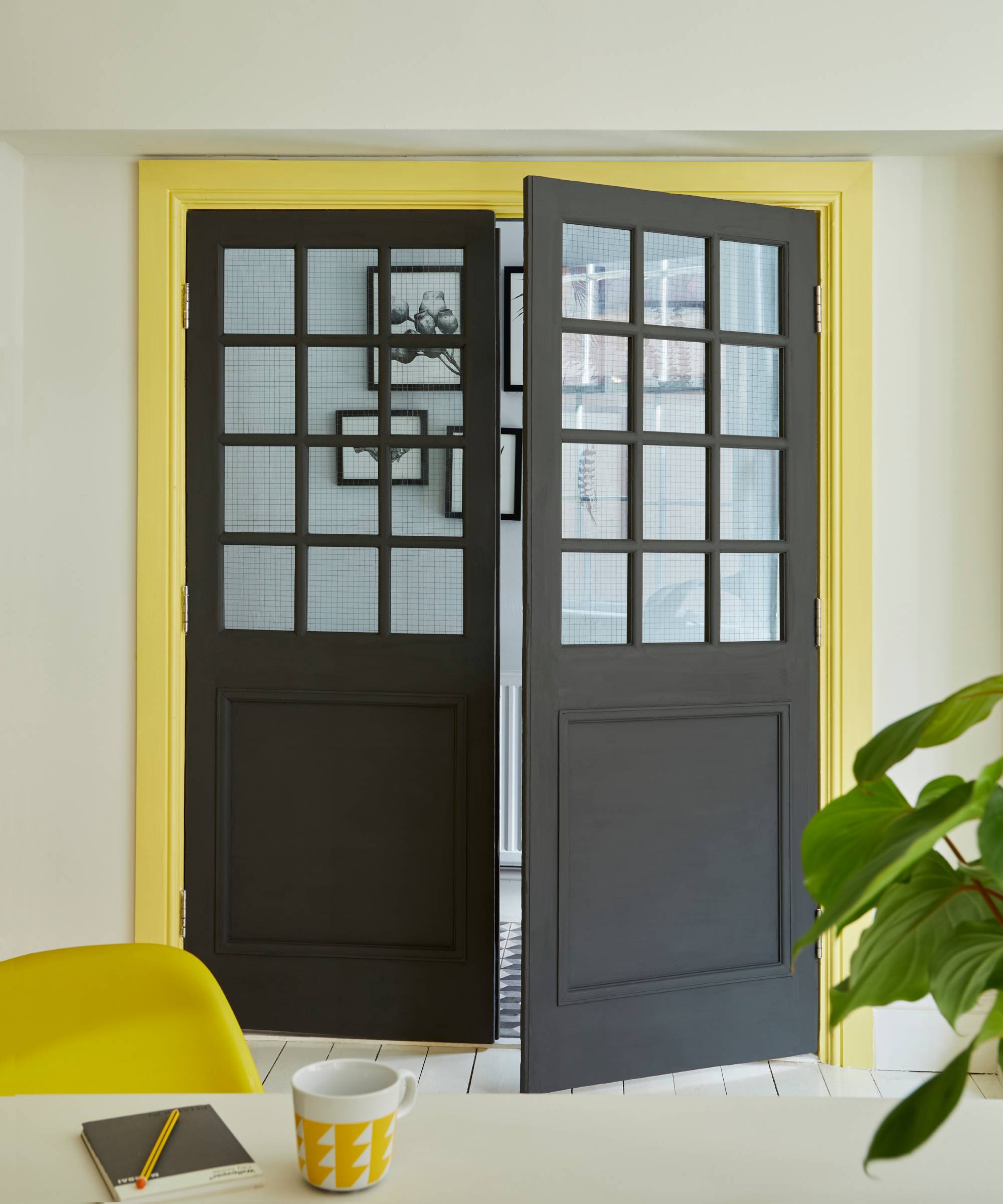 grey double half glazed doors with yellow architrave matching yellow chair in front of table with yellow and white mug and green plant
