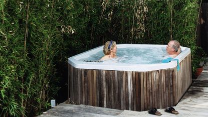 A man and a woman relaxing in a hot tub, set against lush vegetation.