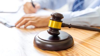 A gavel against the background of a man in a suit doing paperwork.