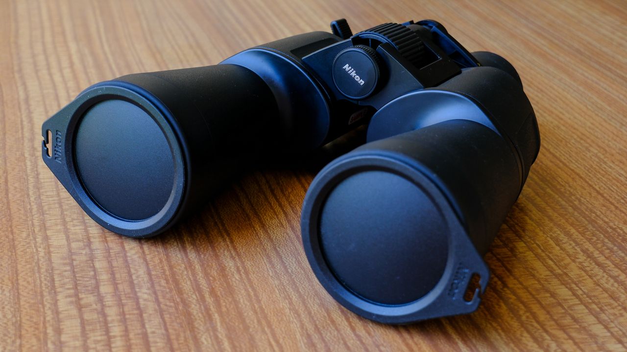 The Nikon Action Zoom 10-22x50 binoculars on a wooden table with lens caps attached.