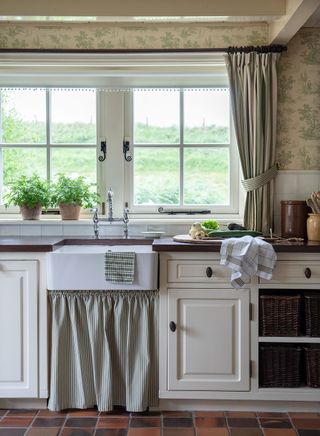 kitchen with butlers sink skirt under units green toile de Jouy wallpaper tiled floor