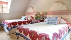 Twin beds with kitsch patterned bedding and headboards. Between the two beds is a shared dusky pink nightstand with a drawer and two colorful lamps