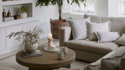 A neutral living room eith a cream corner sofa and a round wooden coffee table