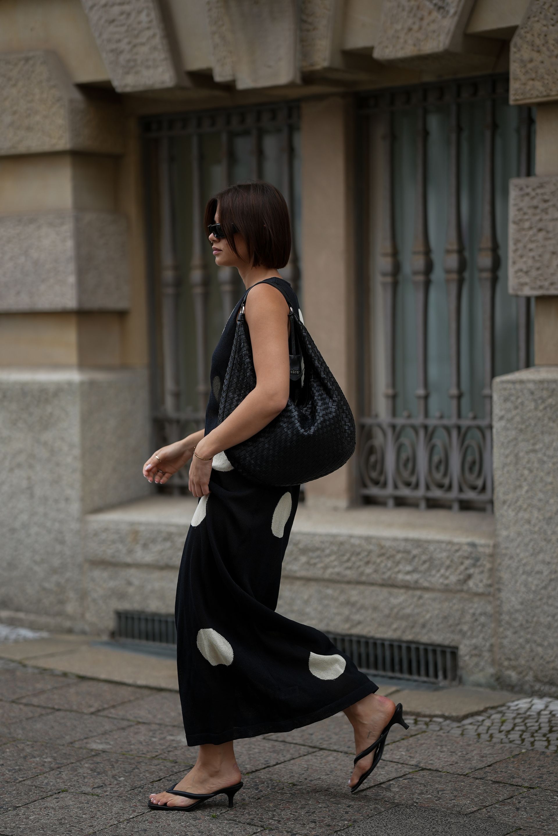 A woman wears a polka dot dress with black kitten heel flip flops.