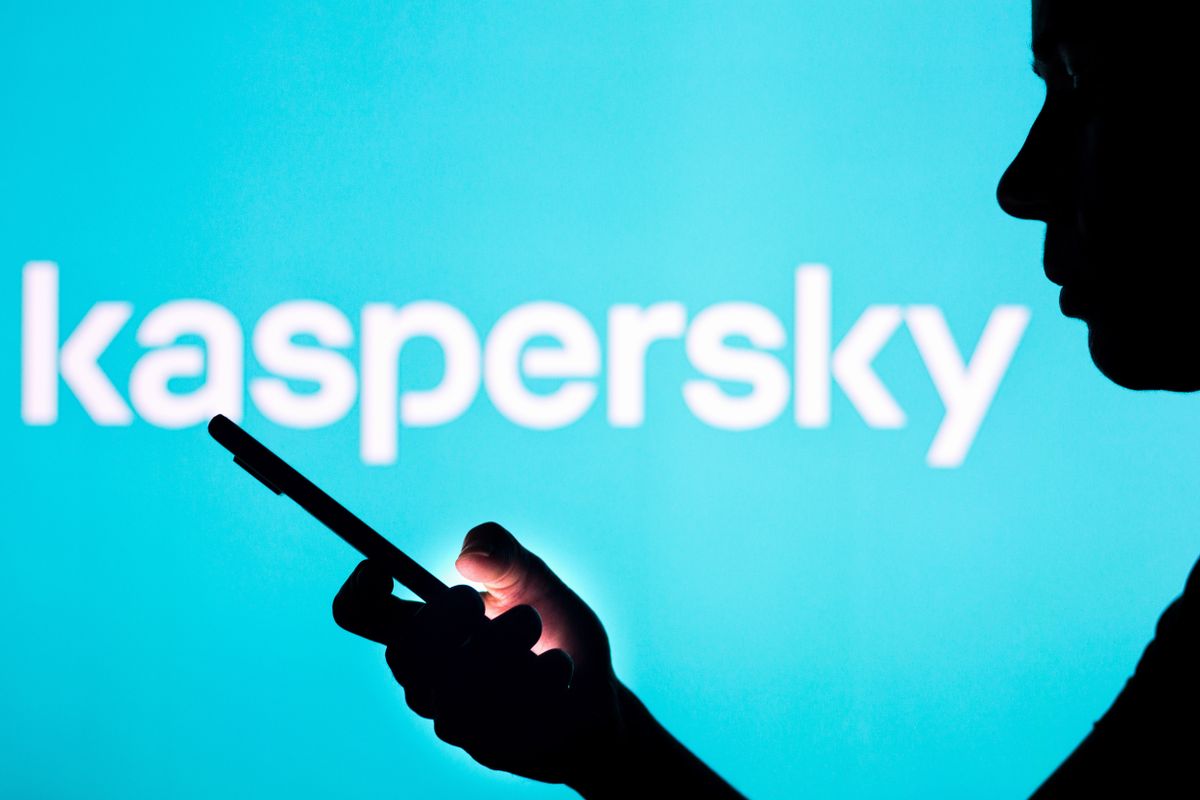 The silhouette of a person looking at their phone, in front of text reading &#039;Kaspersky&#039; on a light blue background.