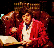 Harry Styles turns his head and winks slowly as he sits in a high back chair holding a pipe.
