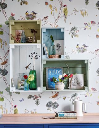 Crate shelving mounted on wall with bird and floral patterned wallpaper