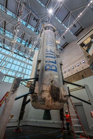 ground-level view, looking up, at a sooty white rocket standing in a white-walled museum hall