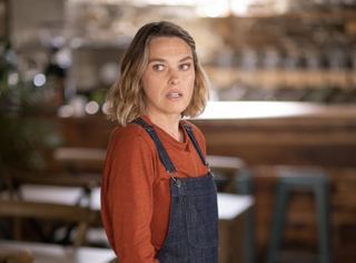 Sally Bretton as Martha Lloyd in Beyond Paradise, standing in her café which can be seen out of focus behind her