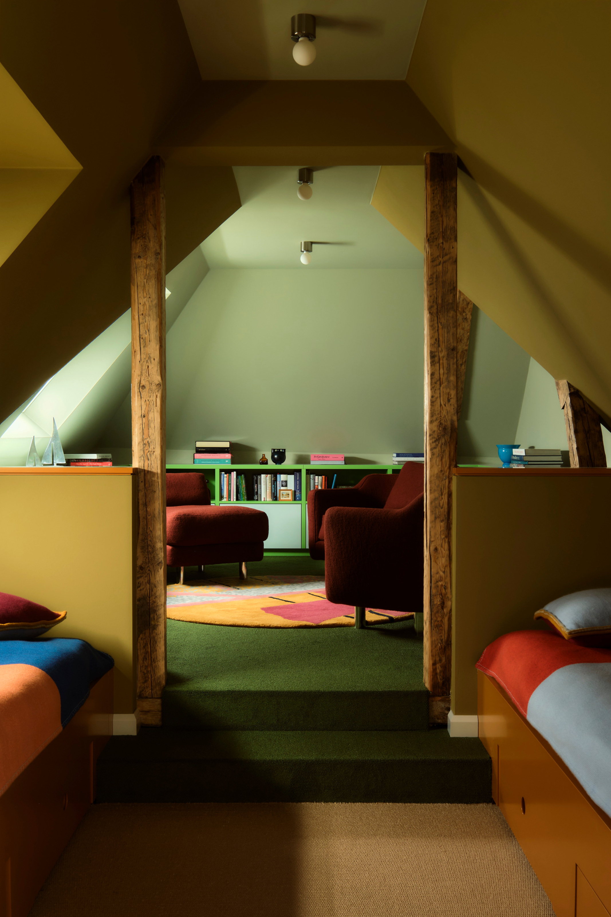 Twin kids' room with ochre walls, orange built-in beds with green carpeted stairs leading to a study area with green shelving and red armchairs
