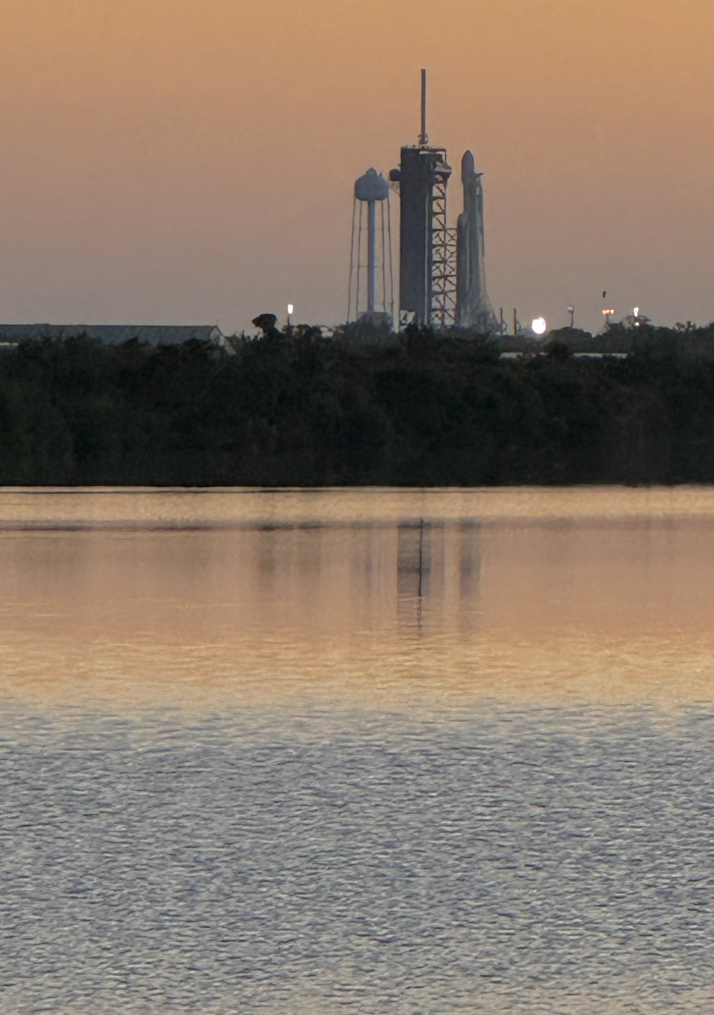 The SpaceX Falcon Heavy rocket on the launch pad at dawn with its reflection in the bay nearby.