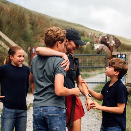 Princess Kate, wore is wearing red shorts and navy baseball cap, is greeted by her three children, Princess Charlotte, Prince George, and Prince Louis, who all wear matching denim jeans