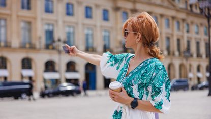 A chic older woman dressed in luxury clothes takes a selfie on a Paris street. She may be new to retirement or on vacation.