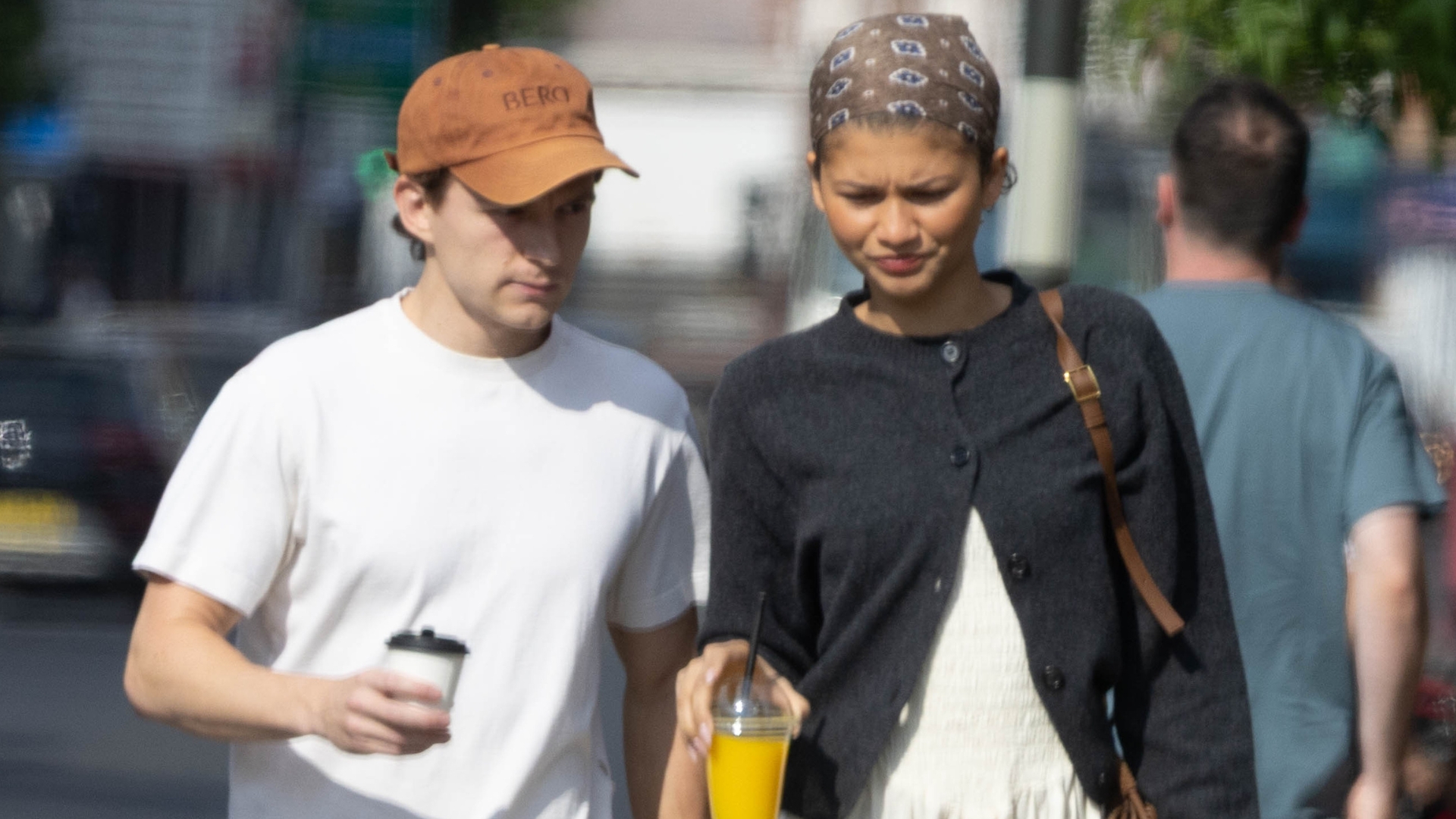 Zendaya walks down the street in London with Tom Holland wearing a white midi dress with a black cardigan, and brown bandana and brown Tabi ballet flats.