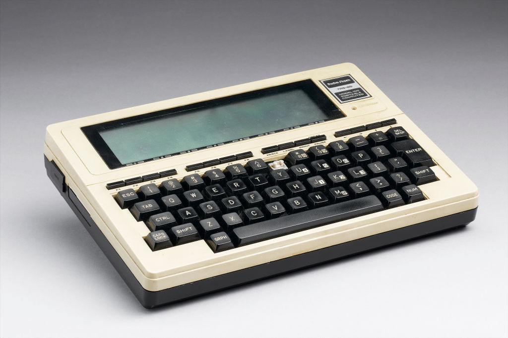 A TRS-80 portable computer, model 100, made by the Tandy corporation, on a grey background.