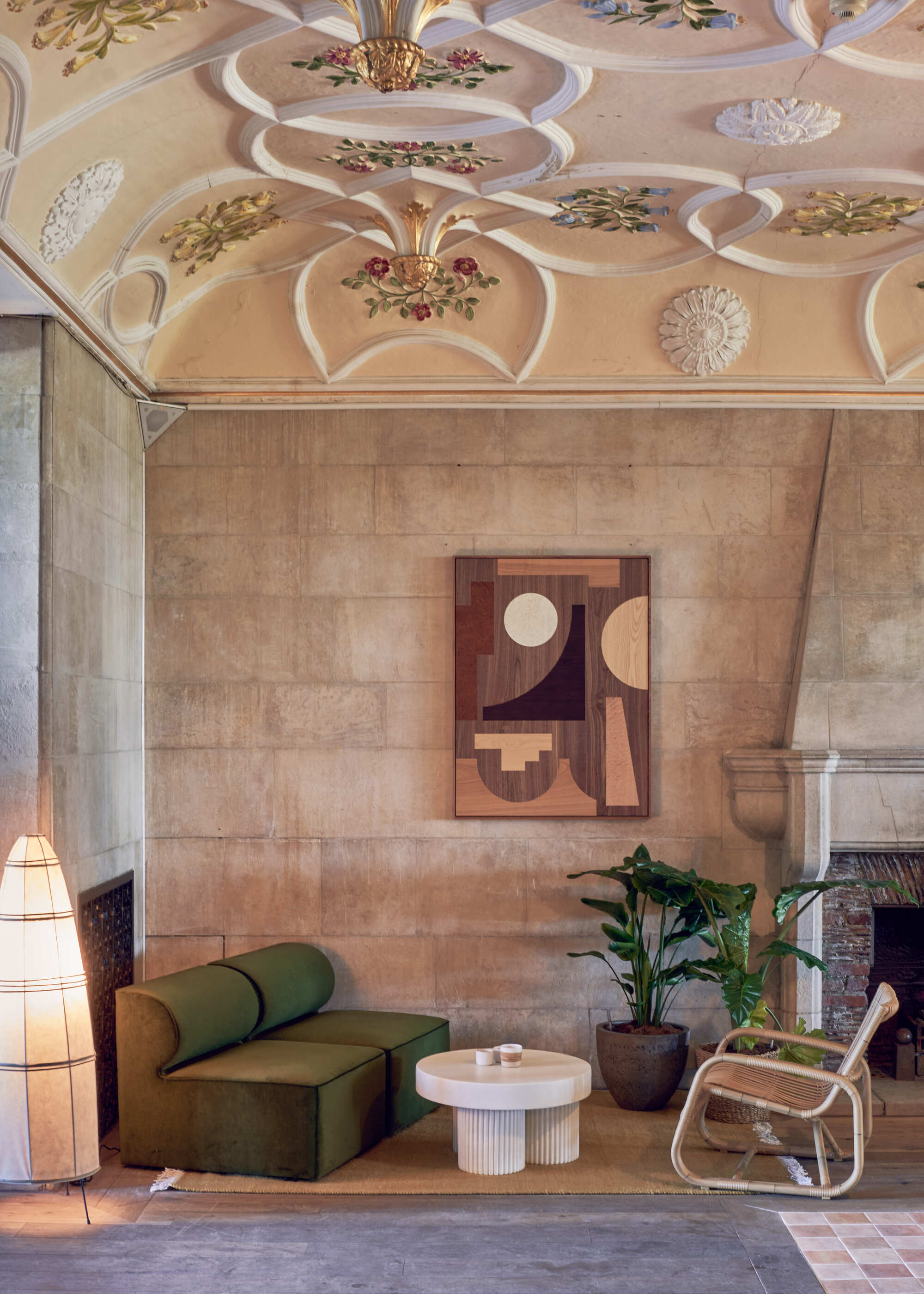 lobby of birch selsdon hotel with sculputral ceiling, stone walls, gray rug, green sofa, rattan chair, white coffee table, potted plant, artwork, and sculptural lamp