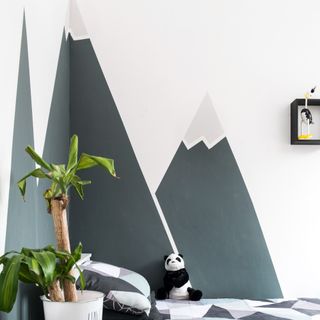 A child's bedroom with a painted wall mural of mountain peaks wrapped around the bed