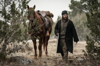 taylor kitsch as isaac reed walking with a horse in american primeval