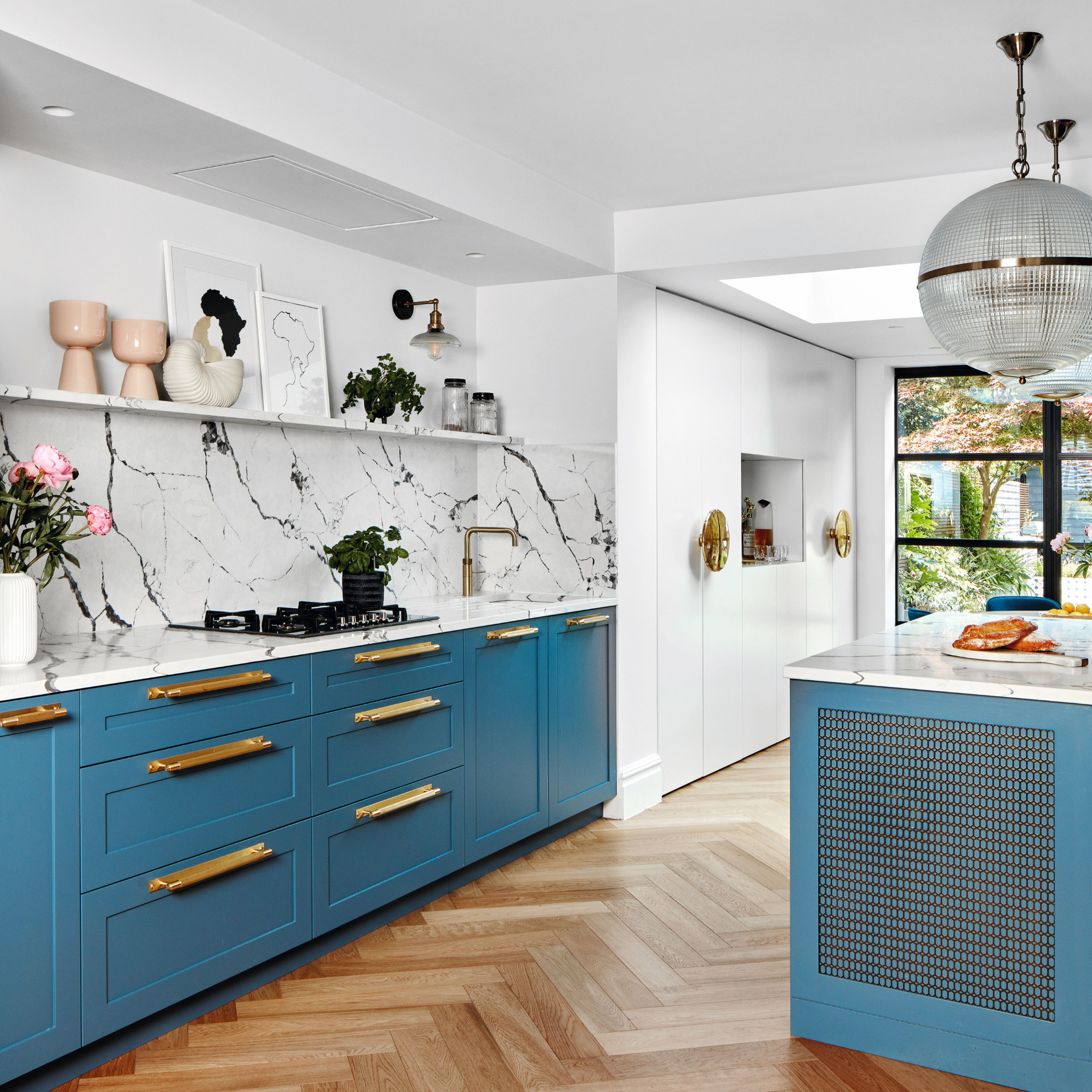 White painted kitchen with marble backsplash, blue painted cabinets and drawers with gold hardware and open shelving