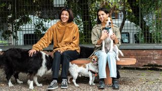 two women sat on a bench with three dogs