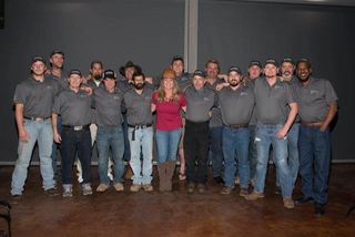 A woman business owner surrounded by employees, all in hardhats