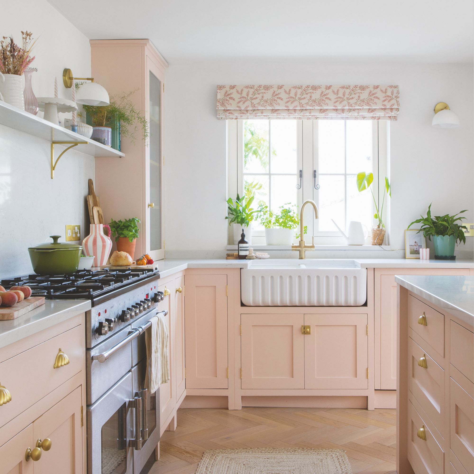 White painted kitchen with baby pink cabinets and a white ceramic sink underneath a window