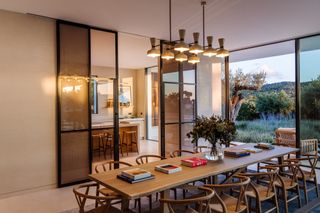 dining room with retro ceiling lights, long rectangular table, designer dining chairs, view through to kitchen, sliding doors and view of outside