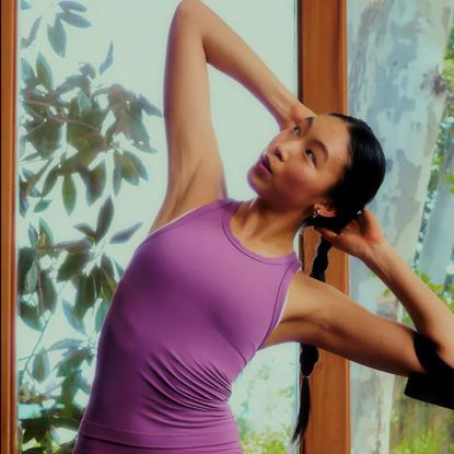Woman wearing purple Lululemon Align tank top during yoga stretch, with plants in background.