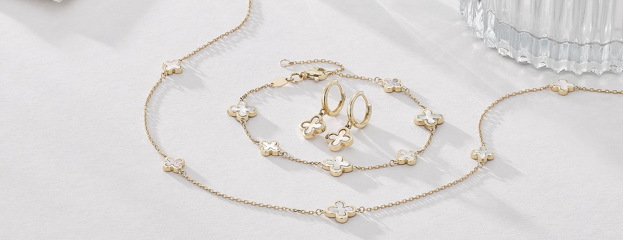 A flat lay image of matching earrings, bracelet and necklace in gold with a white flower detail. 