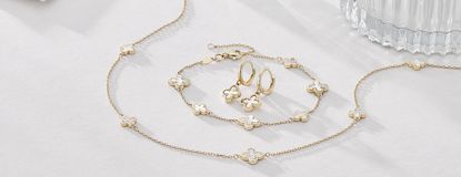 A flat lay image of matching earrings, bracelet and necklace in gold with a white flower detail. 
