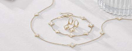 A flat lay image of matching earrings, bracelet and necklace in gold with a white flower detail. 