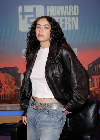 A photo of Charli XCX with long dark brunette curls and a leather jacket.