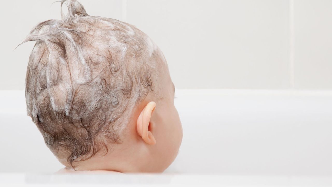 a baby sitting in the bath with shampoo in their hair