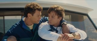 Cooper Koch as Erik Menendez, with his arm around Nicholas Chavez as Lyle Menendez, as they sit on a boat deck in the ocean, in episode 204 of Monsters: The Lyle And Erik Menendez Story.