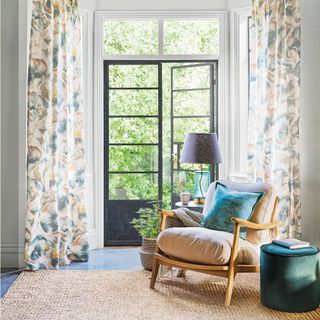 Wood framed armchair in living room by floral curtains