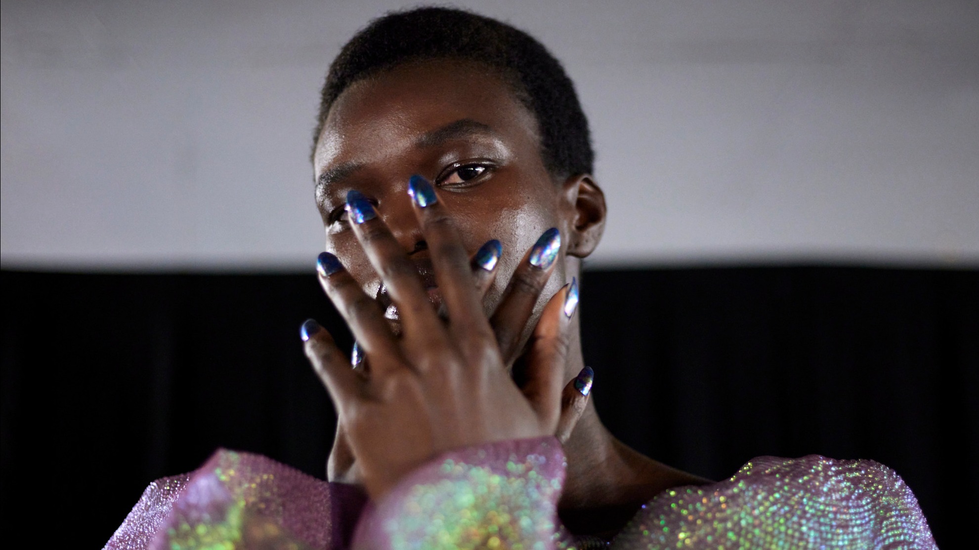 a model wearing metallic blue nail polish and a purple shiny sweater