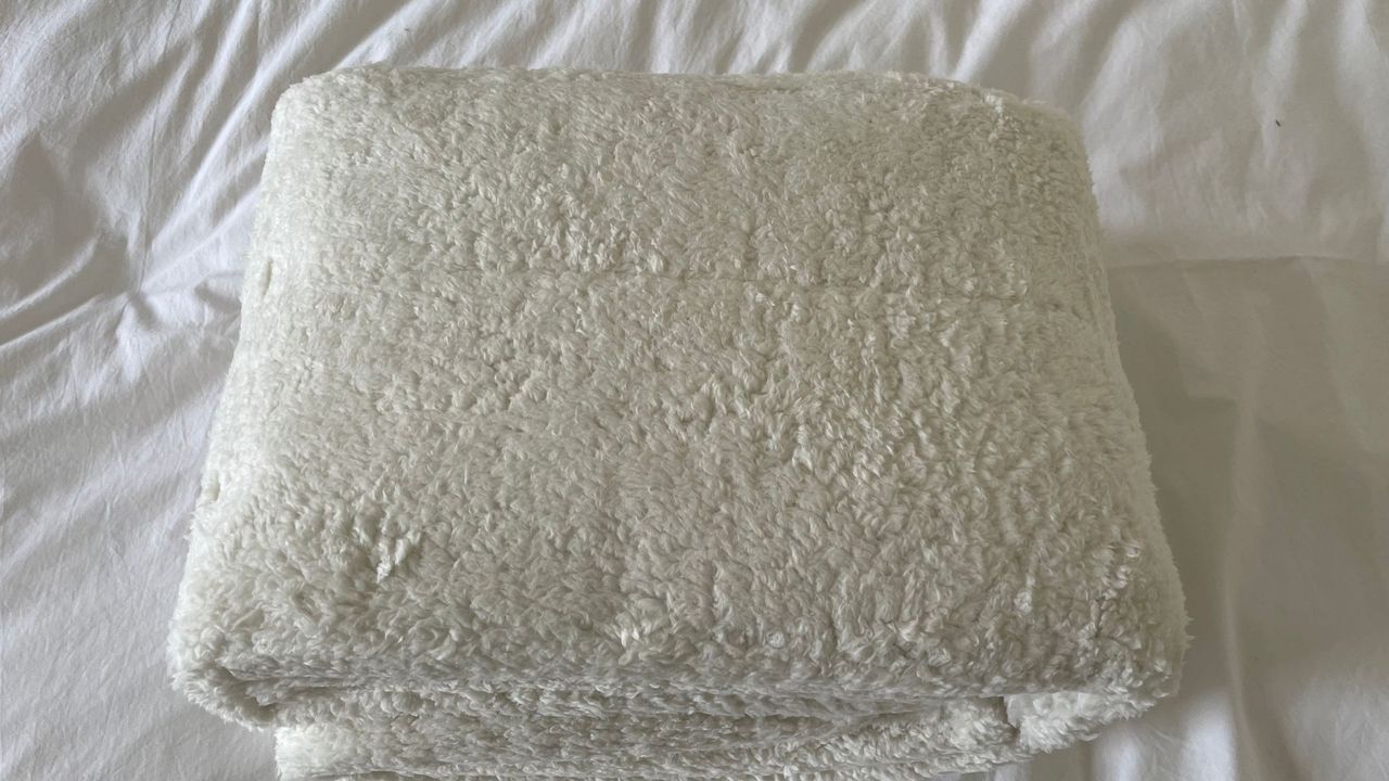 Dreamland Hunker Down Skandi Sherpa Blanket rolled on the bed