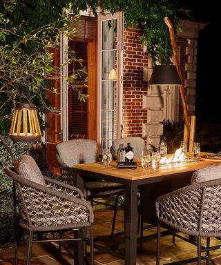 Layered lighting in terrace dining set-up with floor lamp, hanging lantern, and integrated firepit in dining table.