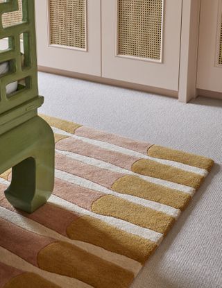 A bedroom with a large beige carpet, and an orange rug