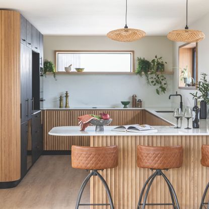 Wooden and black kitchen with marble tops, black accents and brown leather stools around island