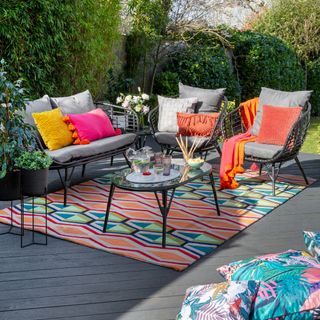 black rattan seating with bright coloured cushions and rug, on decking