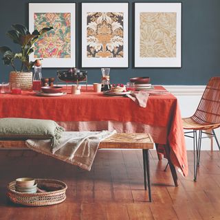 A blue-painted dining room with a layered tablecloth and a throw with a cushion on top of a dining bench