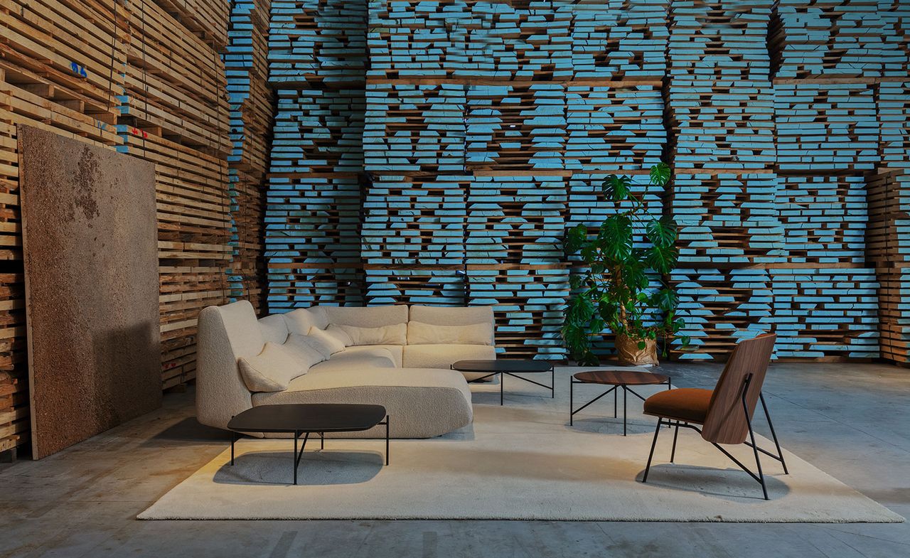 Prostoria showroom interior with walls made of stacked wooden planks. On display is a cream sectional sofa and a modernist upholstered chair with wooden back, shown on a cream area rug