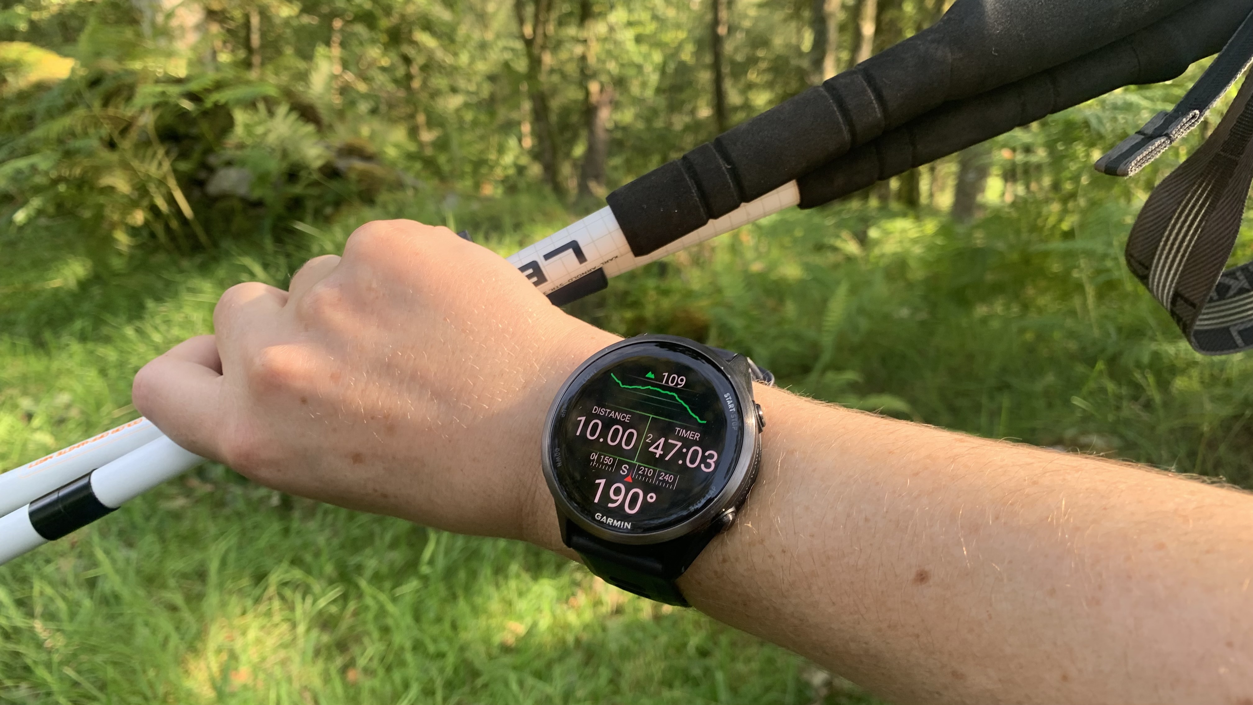 A runner's hand holding trekking poles and wearing the Garmin Forerunner 570